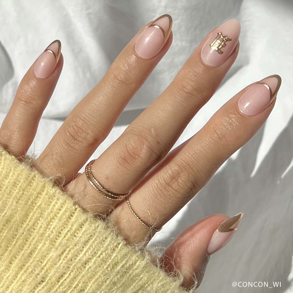 Close-up of a hand with pink nails and gold accents, wearing a yellow sweater.