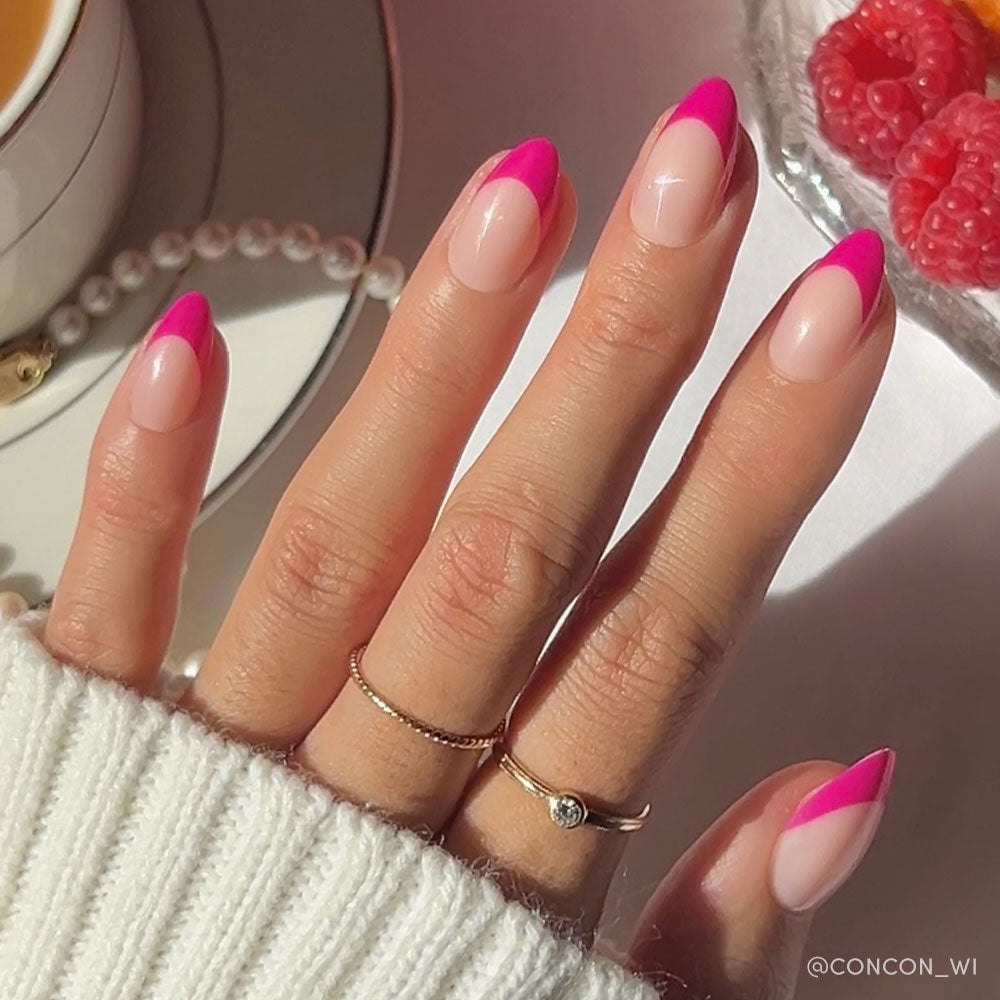 Hand with pink and beige nail polish wearing gold rings, with a blurred background of a cup and berries.