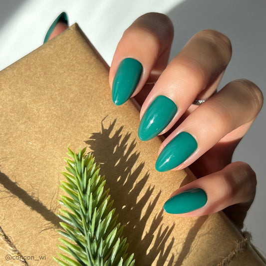 Hand with teal nail polish holding a gold box with a green leaf